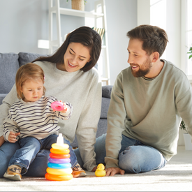 Family playing with colorful toys on a couch in a bright living room.